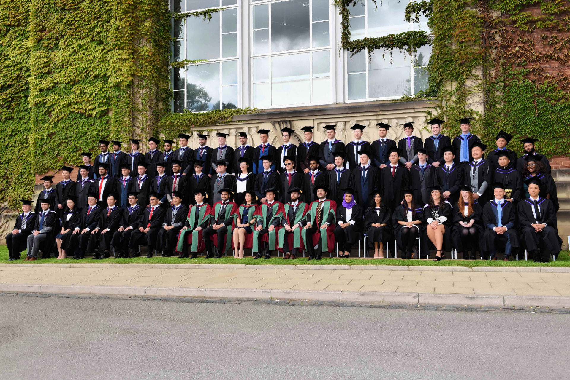 Large graduating class in caps and gowns photographed outside an ivy-covered university building