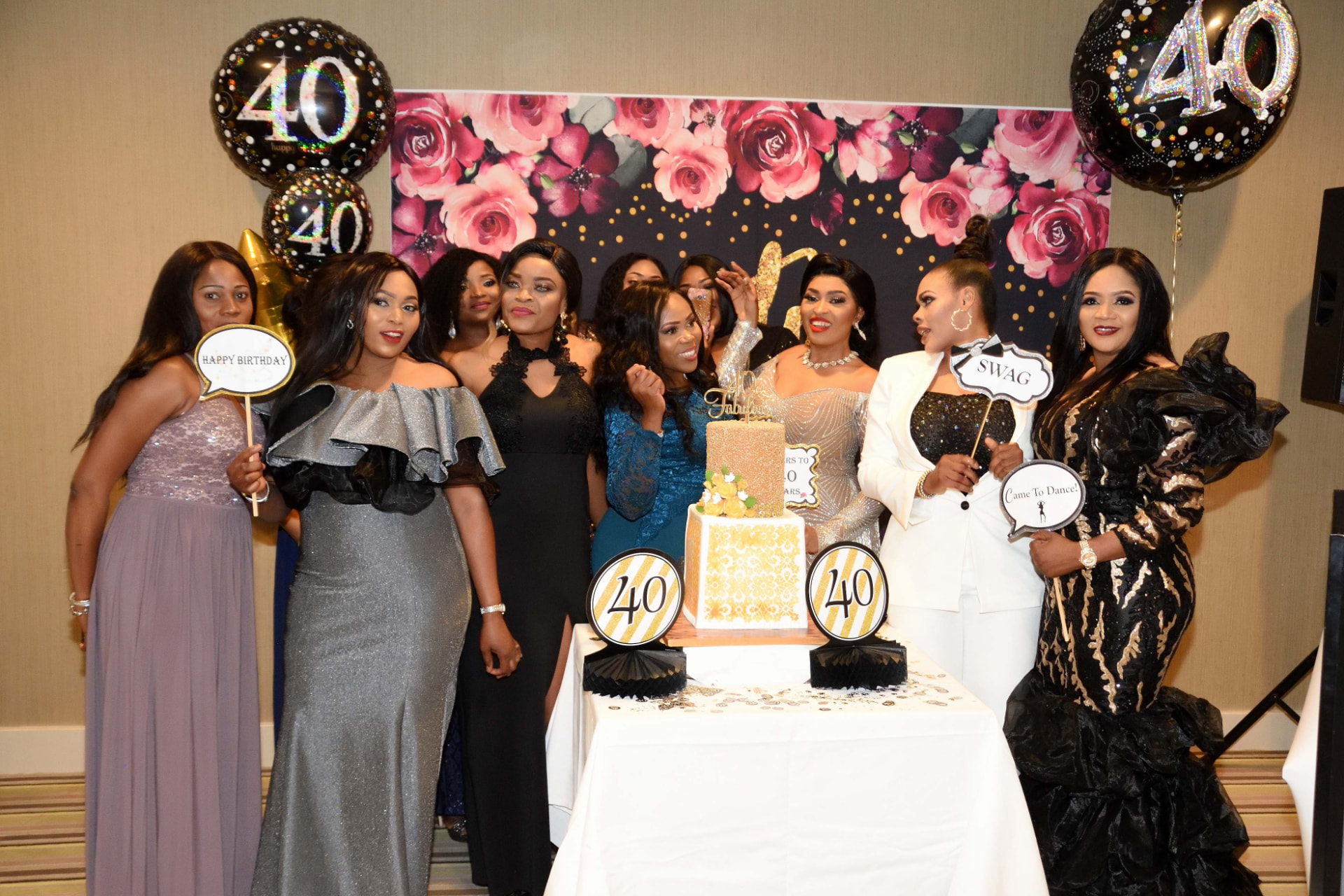 Group of friends in evening gowns celebrating around a gold cake with 40th birthday balloons