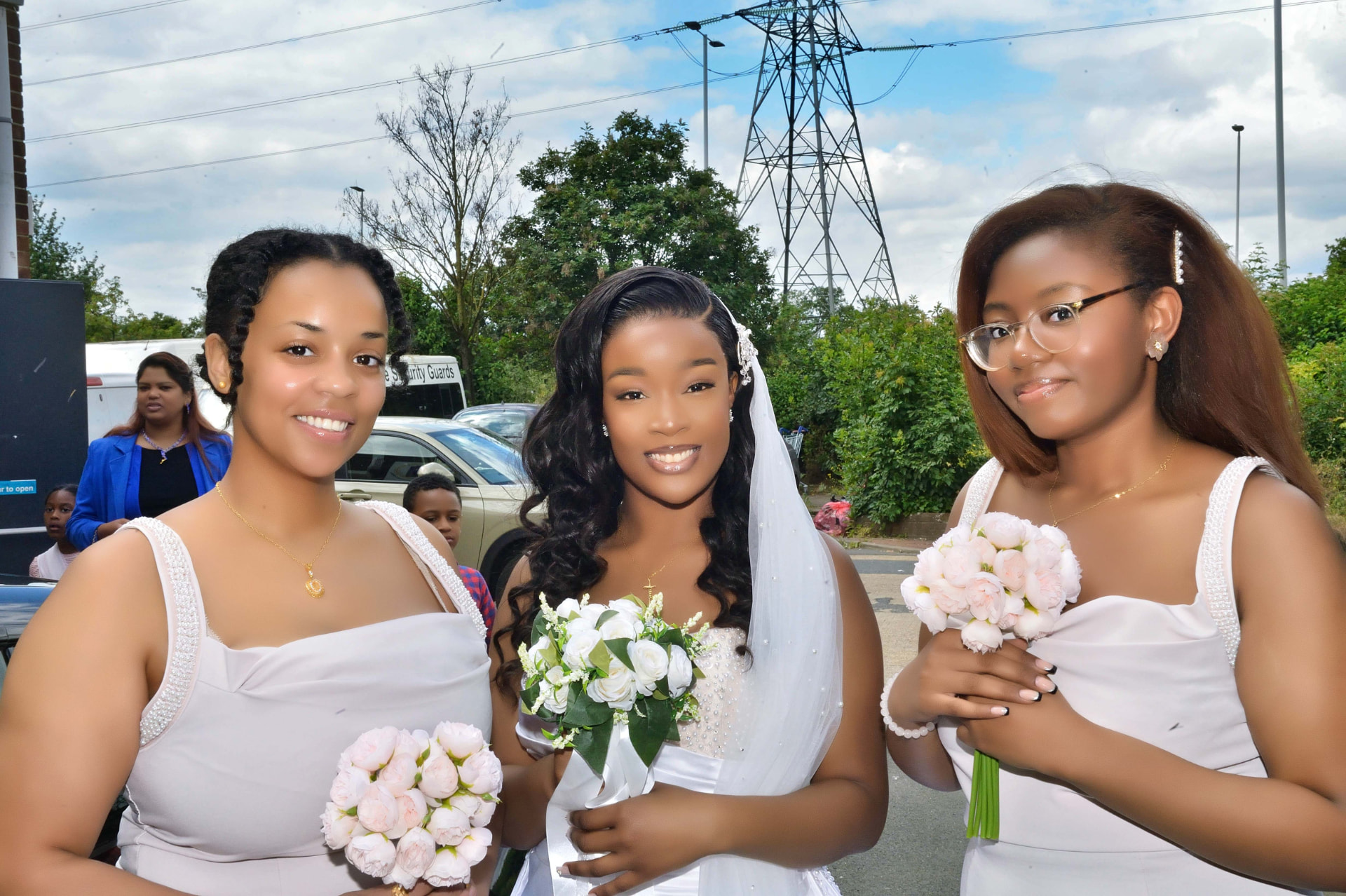Bride in a white gown with two bridesmaids holding pale pink bouquets outside the venue