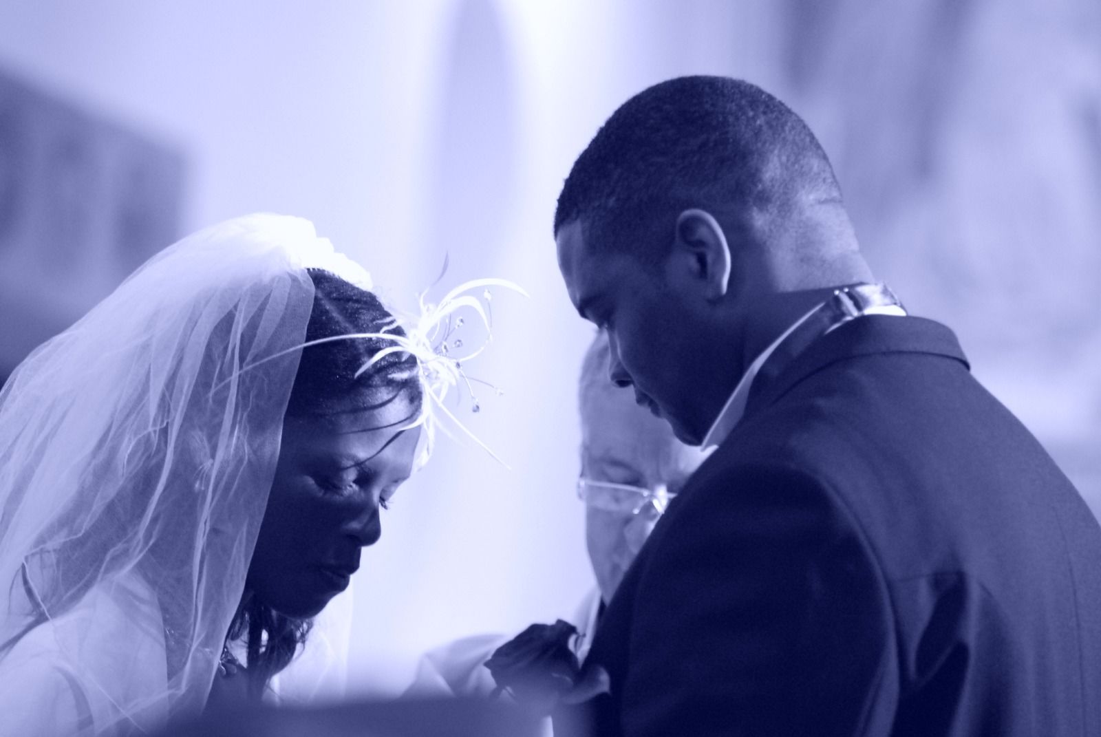 Bride in a veil and groom bowing their heads together in prayer during their wedding ceremony