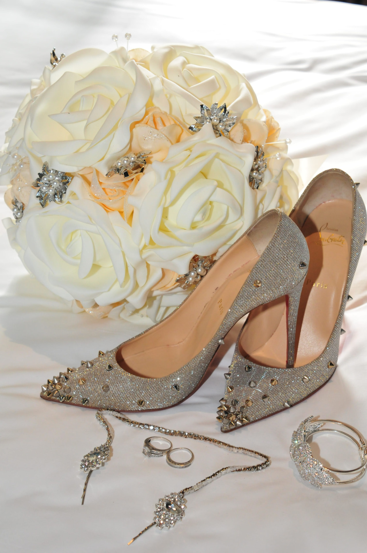 Ivory rose bouquet with crystal brooches beside studded bridal heels, rings and jewellery