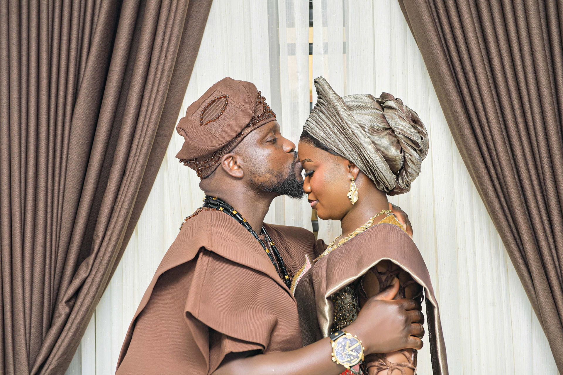 Couple in brown and gold traditional Yoruba attire sharing a tender moment at their engagement ceremony