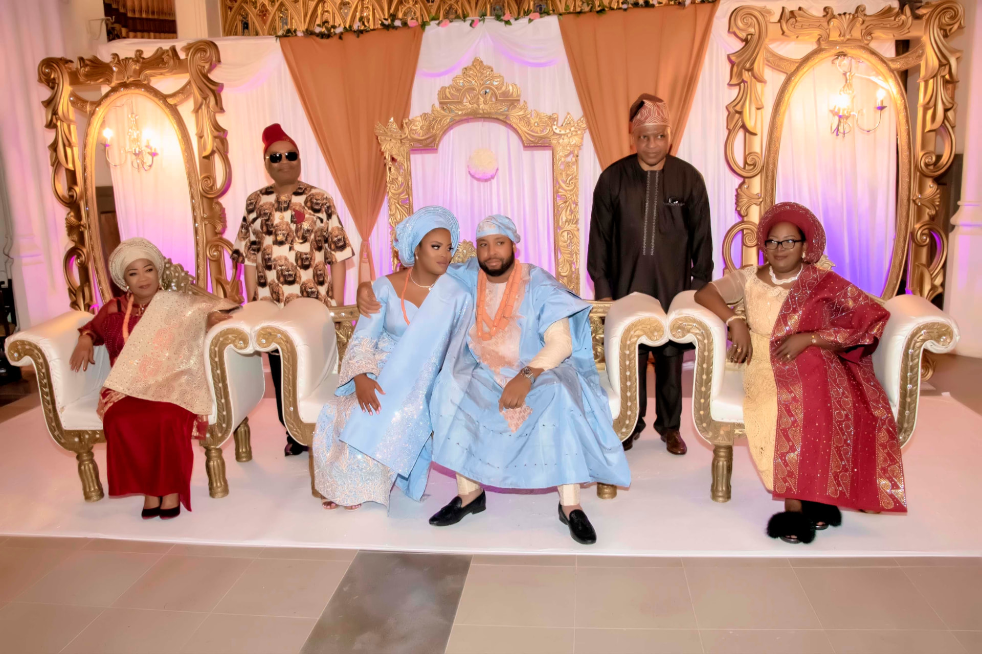 Couple in sky-blue aso-oke seated on gold thrones with both sets of parents at a Nigerian traditional wedding