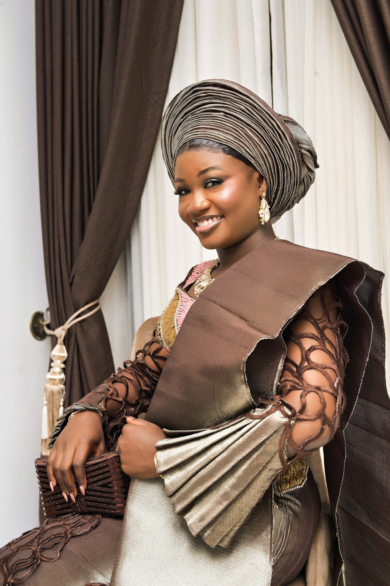 Portrait of a woman smiling in a brown and gold traditional gele and aso-oke outfit