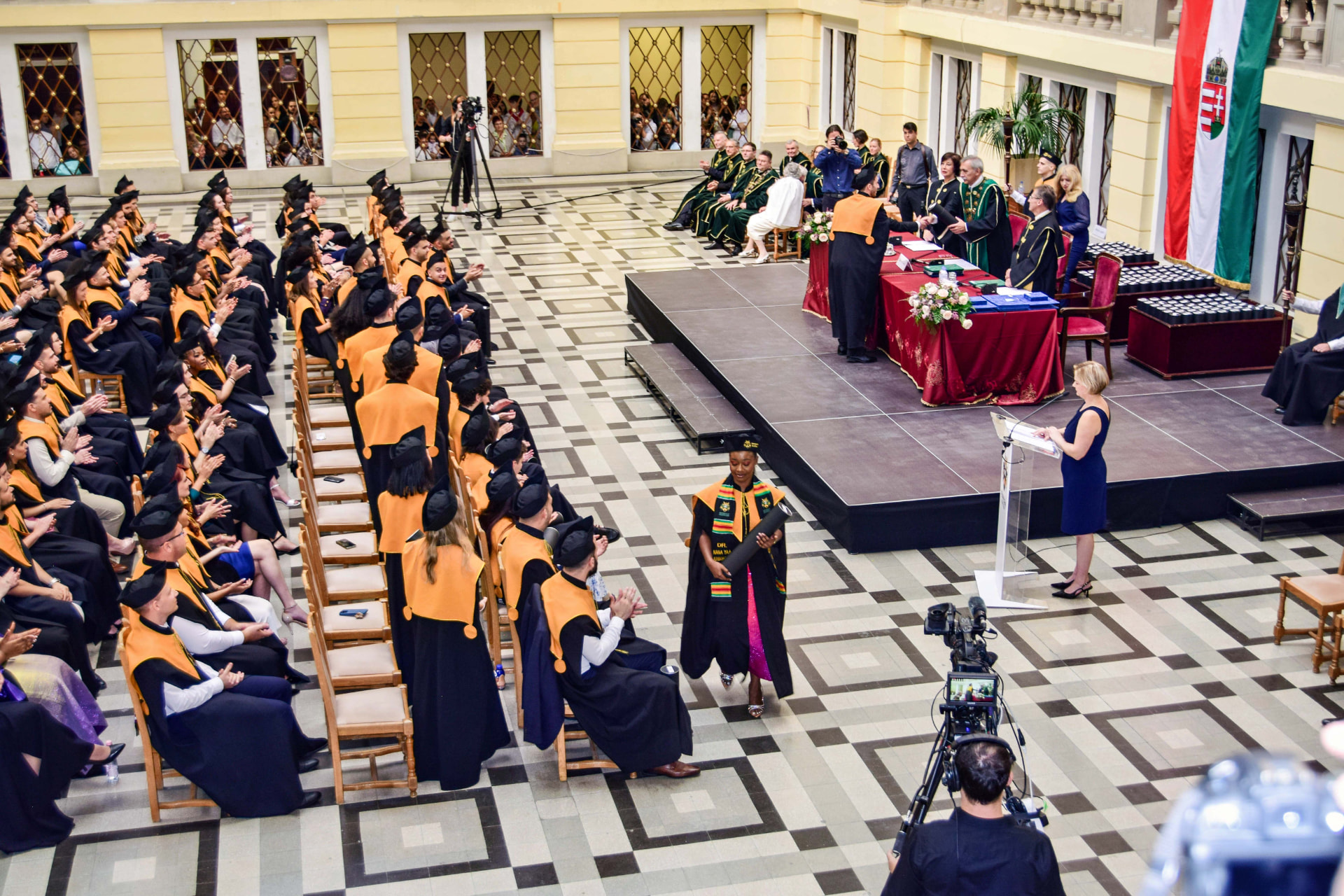 Graduate walking through a convocation hall while POF cameras cover the ceremony